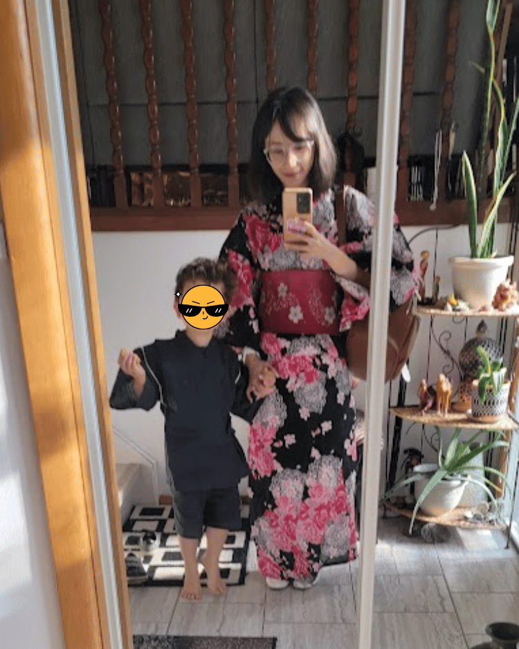 Emi Linds wearing a black and pink floral kimono, holding her son's hand while posing for a mirror selfie