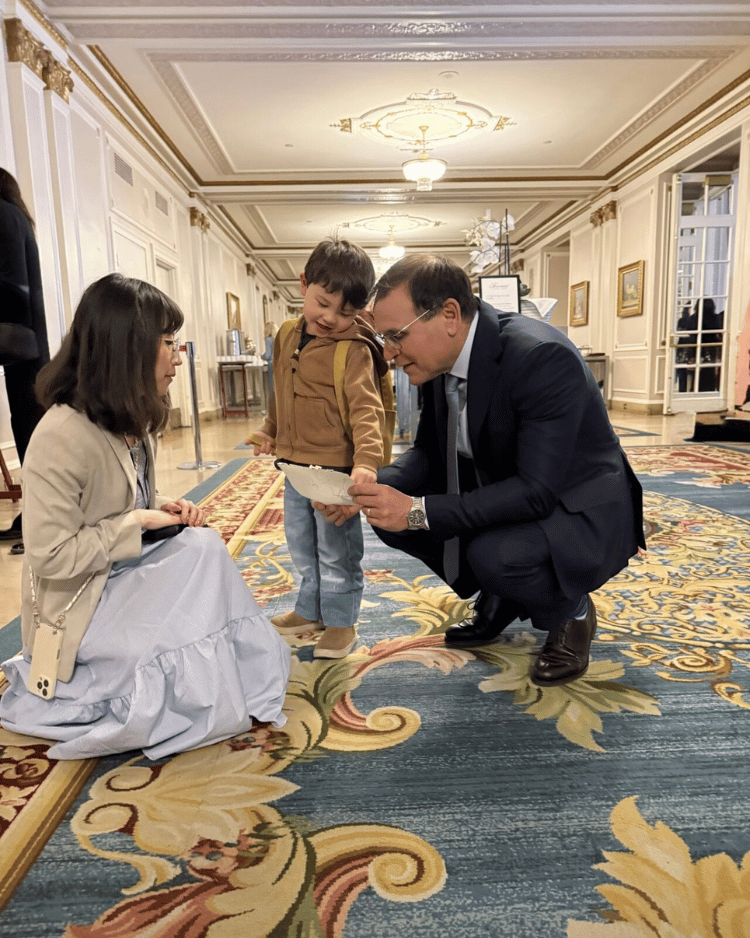 Emi Linds kneeling beside her son while speaking with Canadian Senator Leo Housakos in a formal hallway